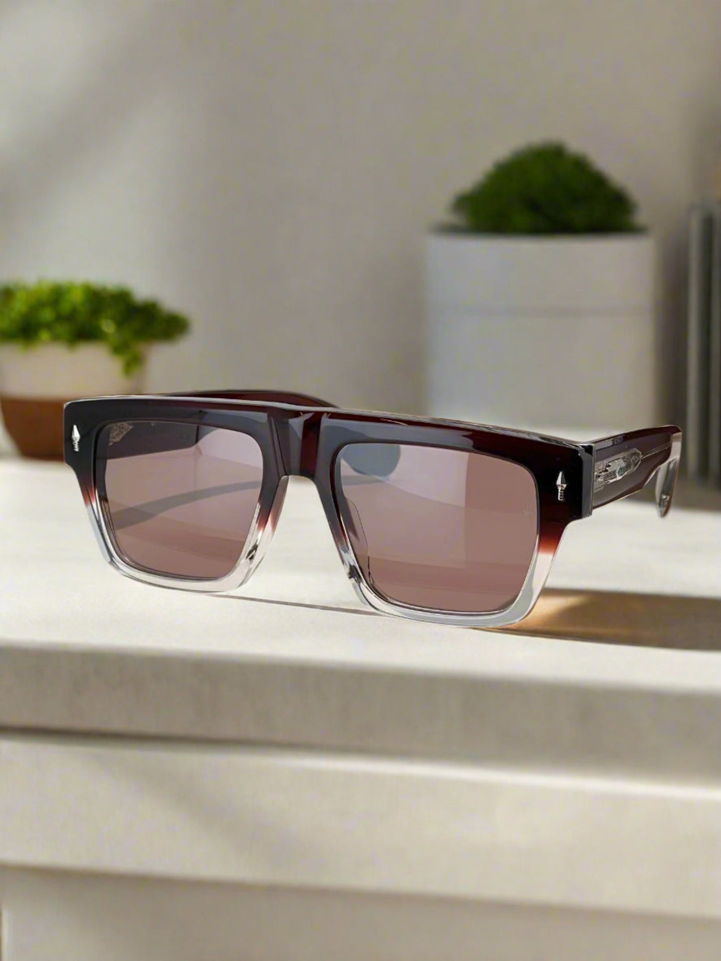 Sunglasses with a brown gradient lens on a reflective surface, with a brand box in the background.