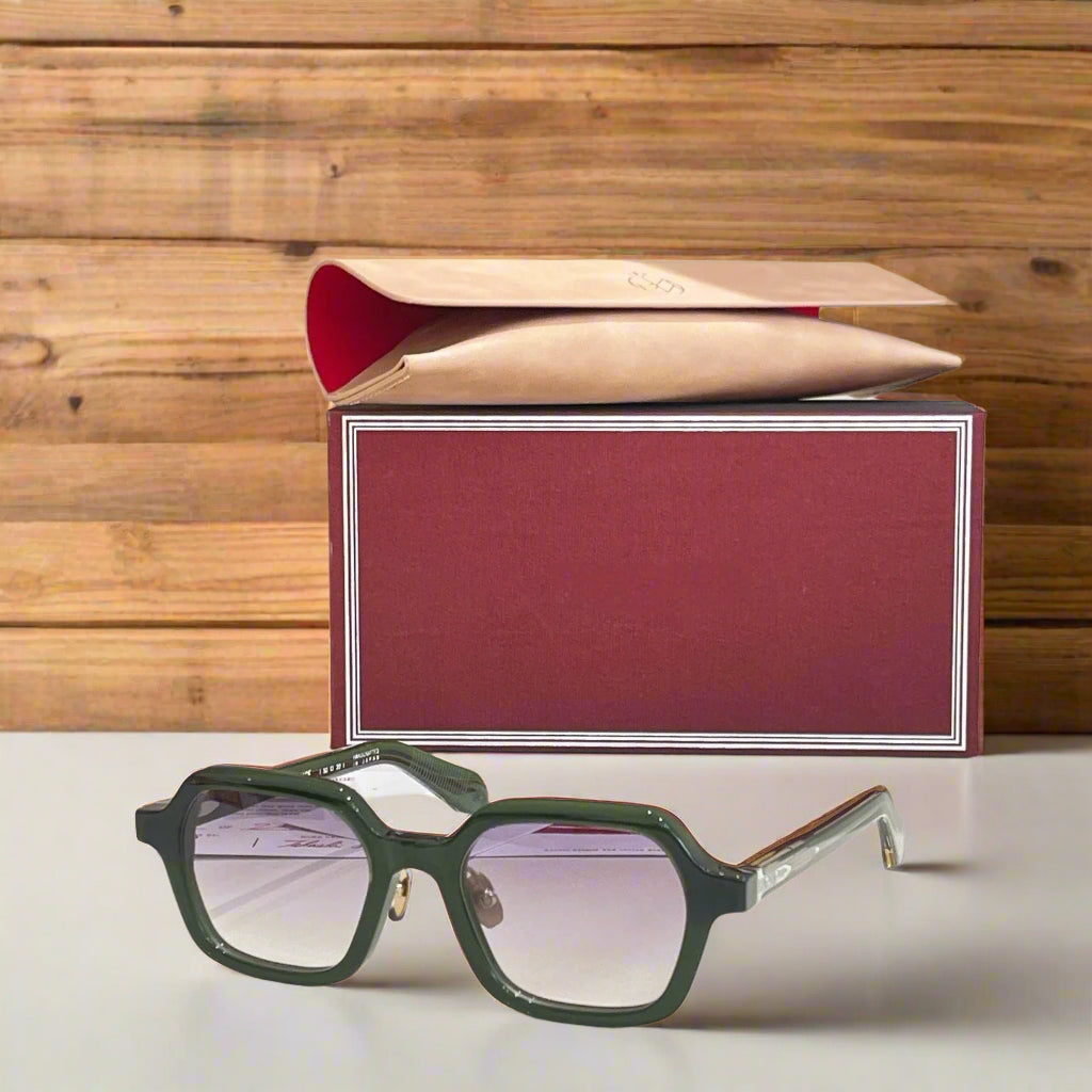 Green sunglasses with a red and gold box on a white surface