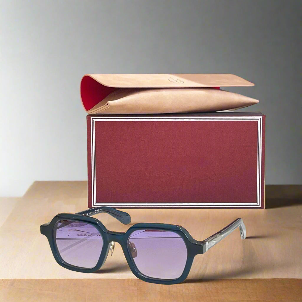 Sunglasses with purple lenses on a white surface next to a red and beige box.