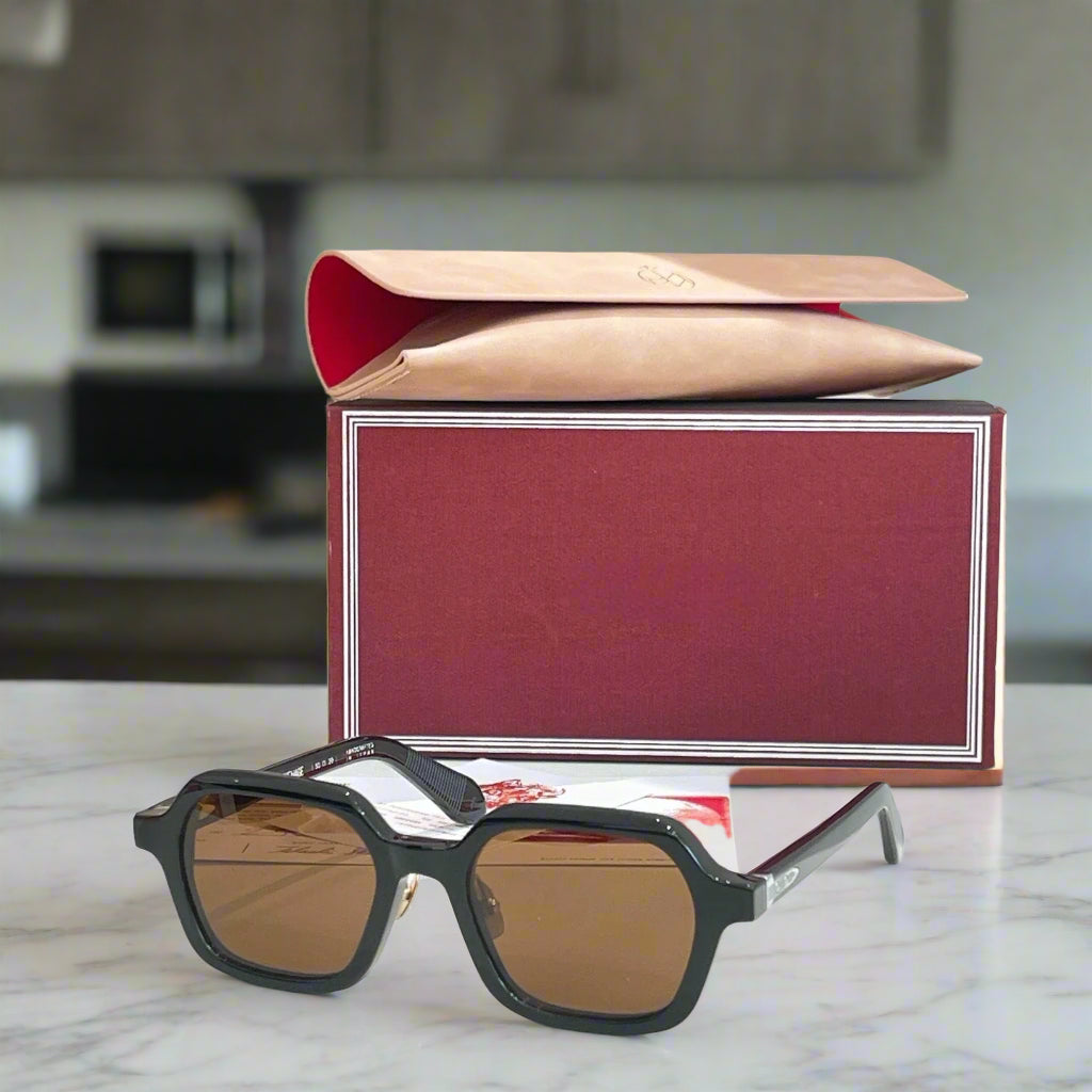 Black sunglasses with brown lenses on a reflective surface in front of a red and beige box.