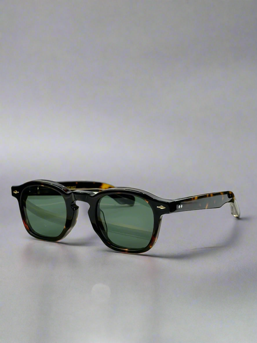 Sunglasses with tortoiseshell frame and green lenses on a gold display stand, with a ZEPHIRIN branded box in the background.