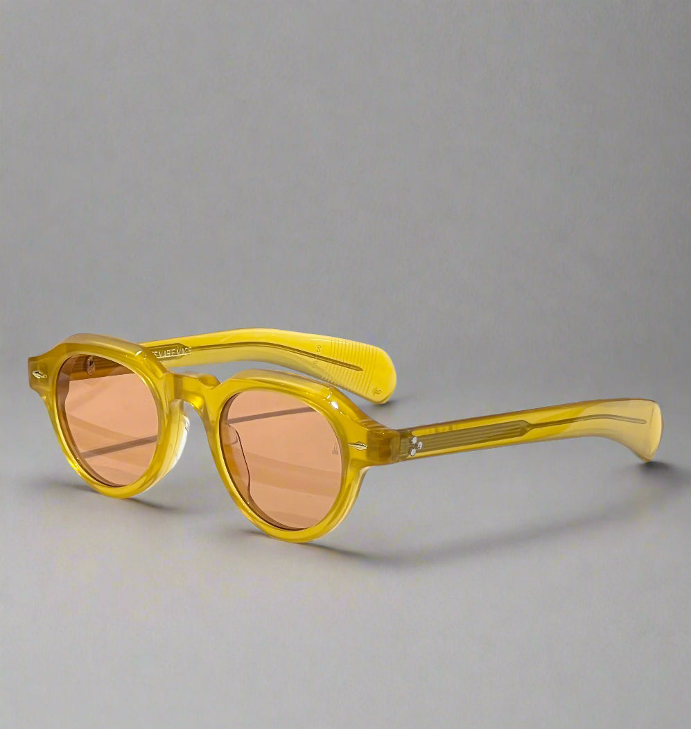 Yellow sunglasses with brown lenses on a white surface with a branded box in the background.