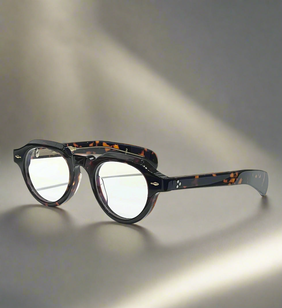 Round eyeglasses with tortoiseshell pattern on a white surface with a branded box in the background.