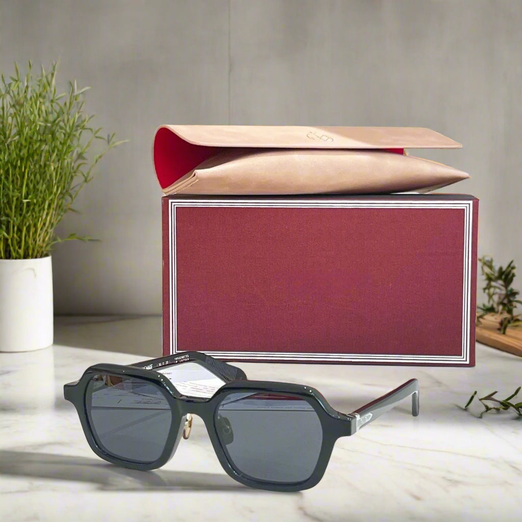 Black sunglasses with a red and beige box on a light surface