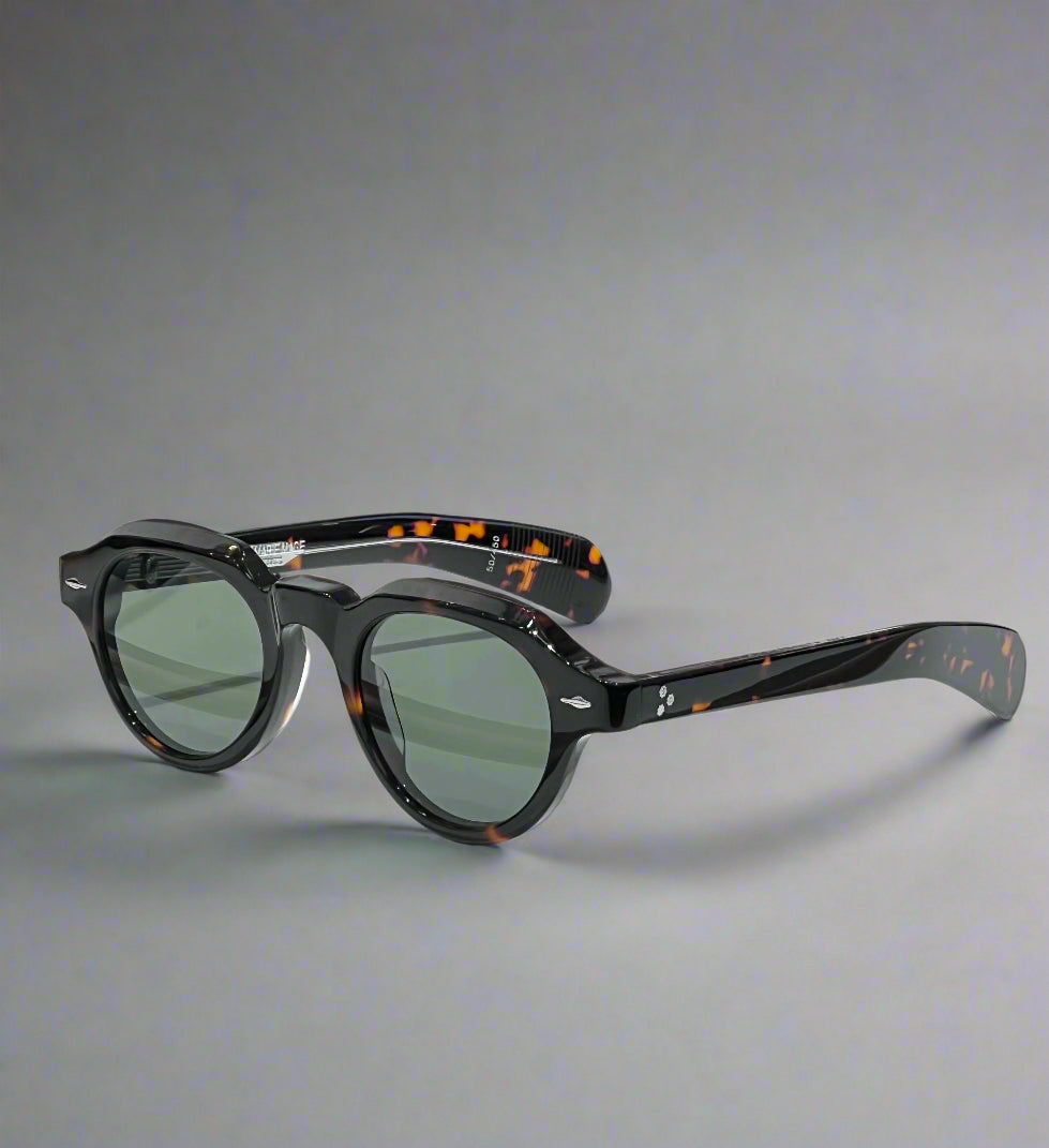 Sunglasses with tortoiseshell frame and green lenses on a wooden surface with a branded box in the background.