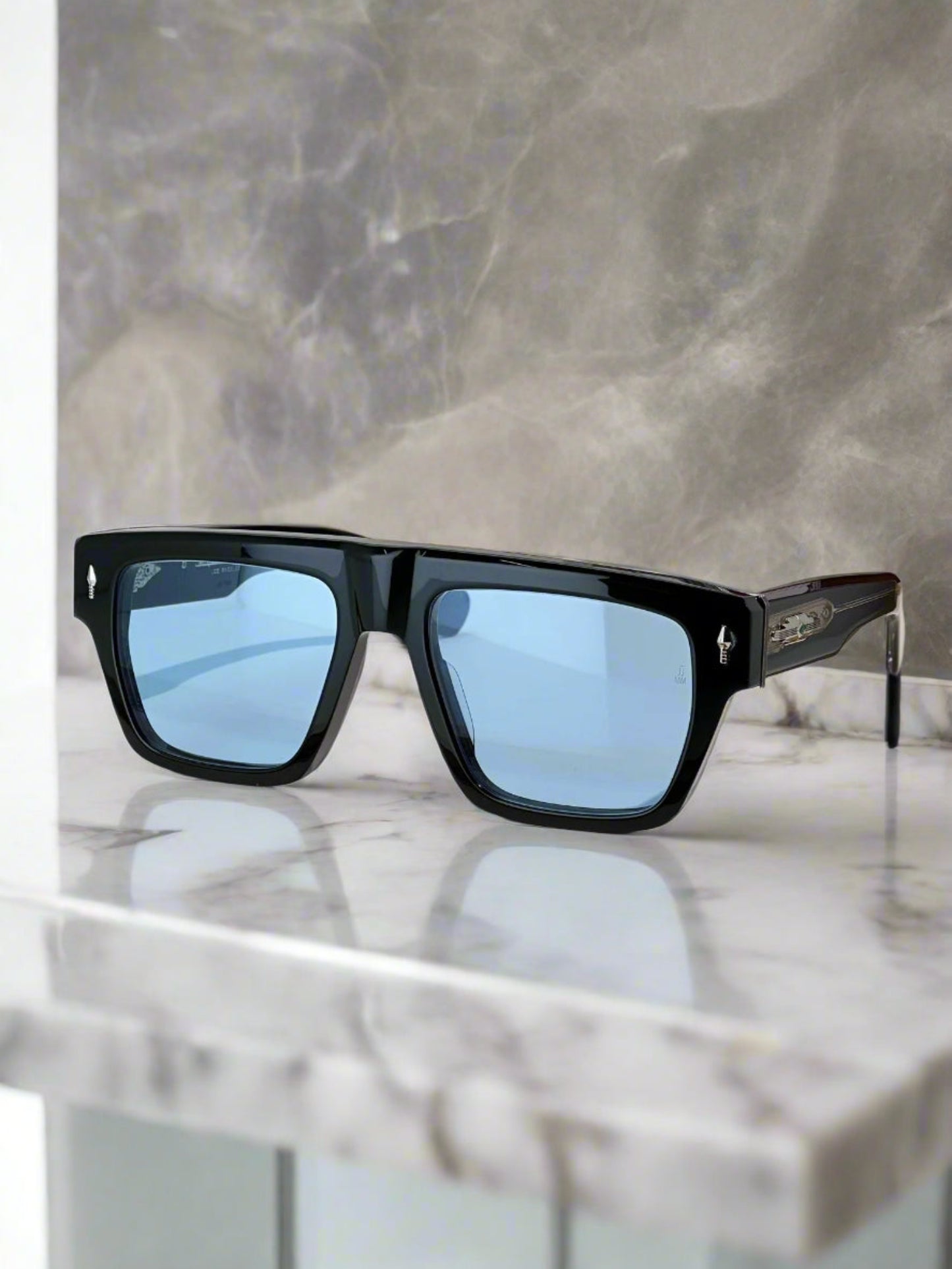Black sunglasses with blue lenses on a wooden surface, with a branded box in the background.