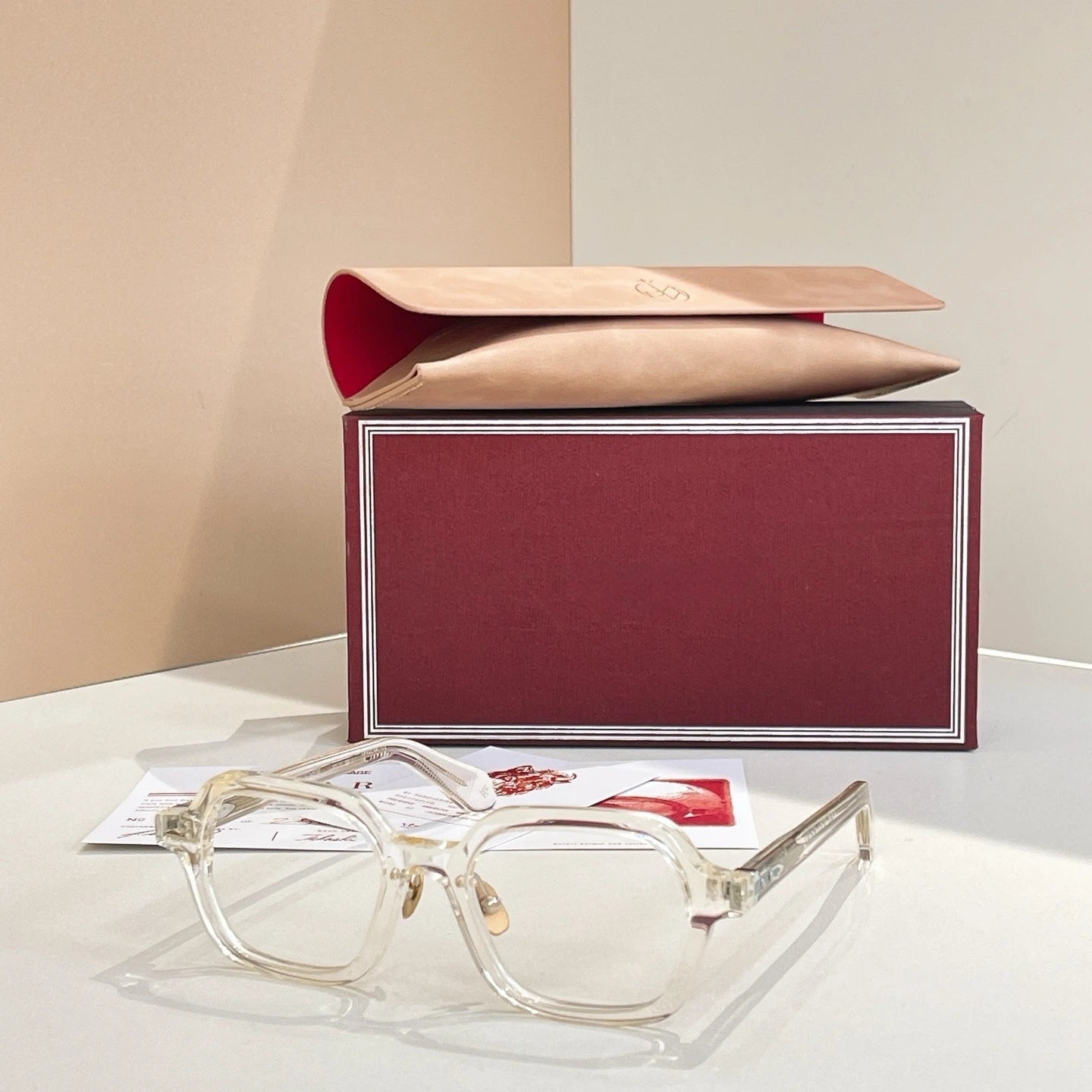 Clear eyeglasses with gold accents on a white surface next to a branded box.