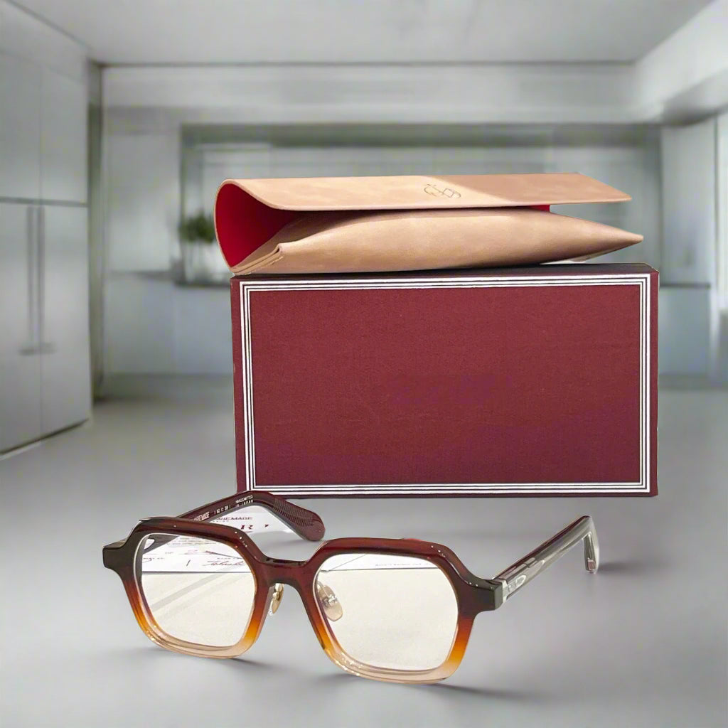 Brown eyeglasses on a white surface with a maroon box in the background