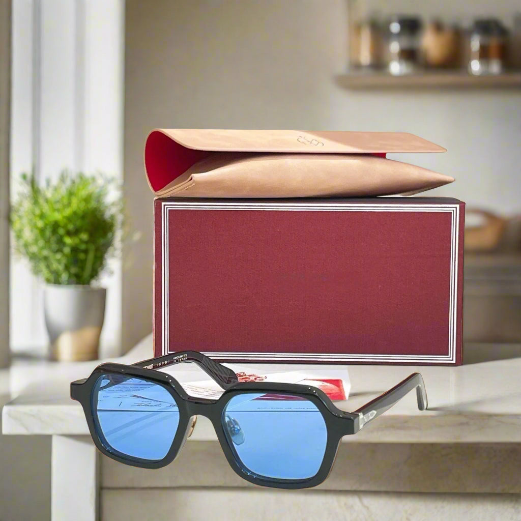 Black sunglasses with blue lenses on a white surface next to a red and gold box.