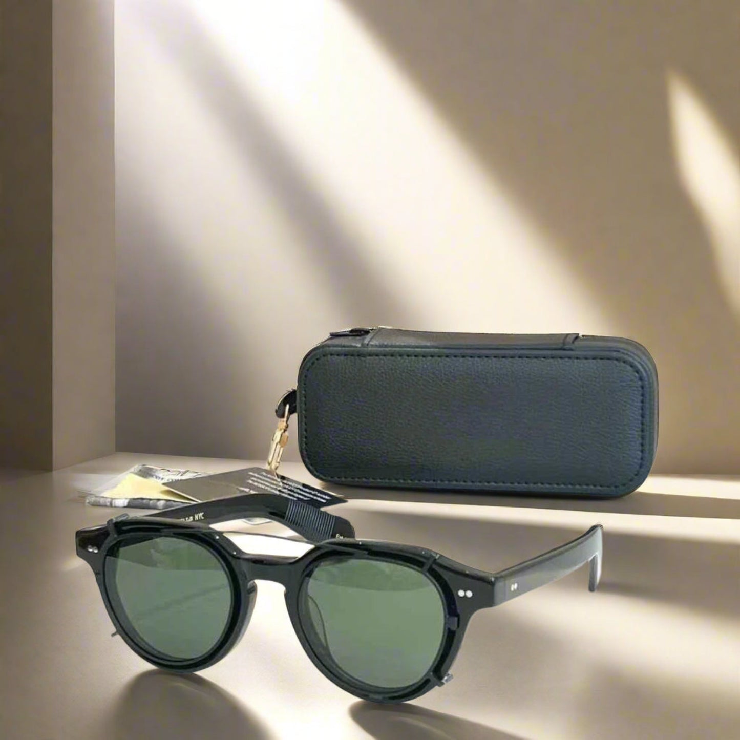 Black sunglasses with green lenses on a reflective surface next to a black case.