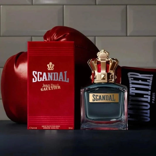 Scandal Jean Paul Gaultier perfume bottle and packaging on a gray surface with a brick wall background.